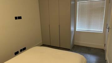 Un dormitorio con una cama, un armario, una ventana con persianas y una puerta.