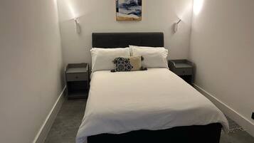 Un dormitorio con una cama, dos mesitas de noche, una lámpara de pared y un cuadro sobre la cama.