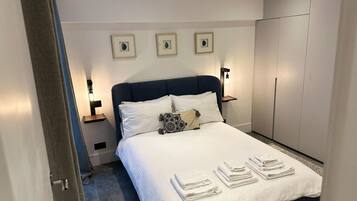 A hotel room with a bed, bedside lamps, a wardrobe, and artwork on the wall.