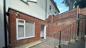 Une façade en briques, un escalier en métal et une entrée fermée par un portail.