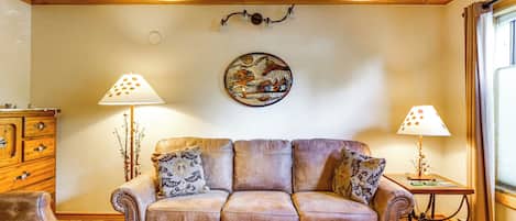 A living room with a brown leather sofa, two lamps, a decorative wall piece, and a wooden cabinet.