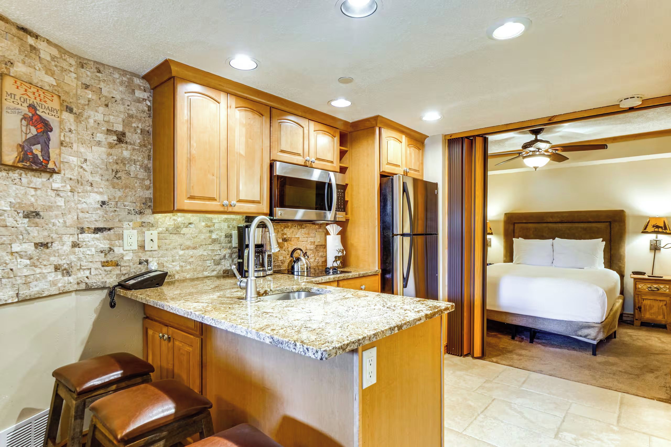 A kitchen with granite countertops, wooden cabinets, a stainless steel refrigerator, and a microwave.