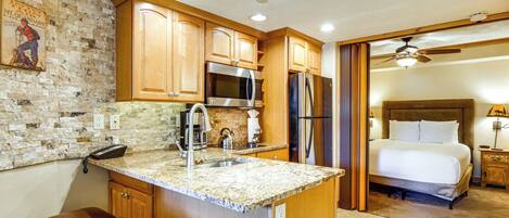 A kitchen with granite countertops, wooden cabinets, a stainless steel refrigerator, and a microwave.