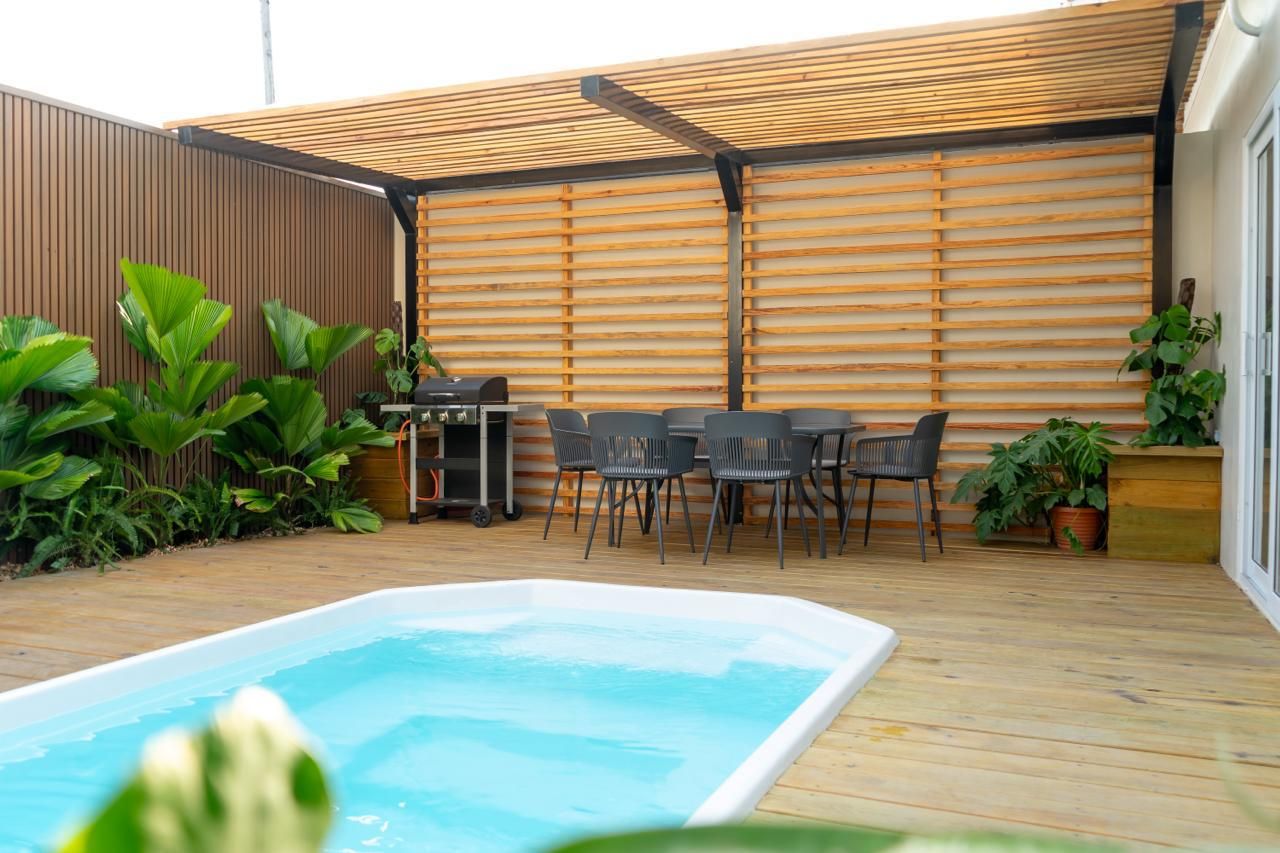A wooden deck with a swimming pool, outdoor seating, and a grill area.
