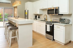 A modern kitchen with white cabinets, a stainless steel refrigerator, a microwave, a stove, and a toaster.