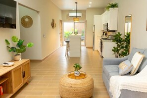 Una sala moderna con sofá, mesa de centro y televisión. Cuenta con una zona de cocina con armarios y microondas.