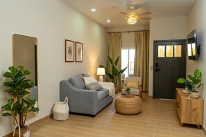 A living room with a sofa, a coffee table, a lamp, and a television on the wall.