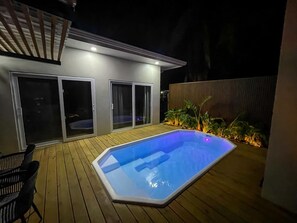 Una piscina con muelle de madera, un porche cubierto y un ventanal corredera que da a una zona exterior techada.