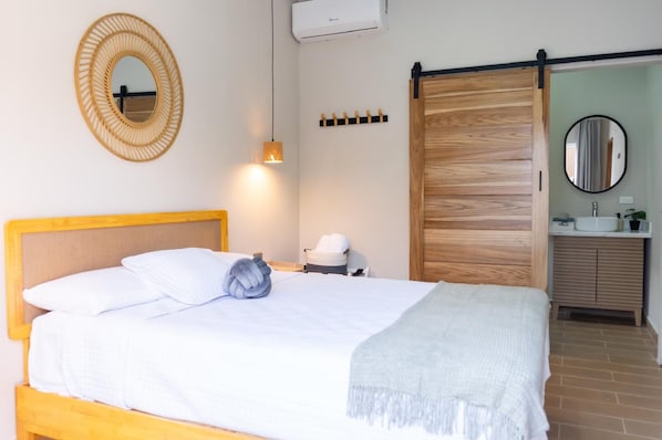 A hotel room with a bed, a bedside lamp, a wall-mounted mirror, a sliding door, and a bathroom with a sink and mirror.
