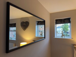 En spegel som reflekterar en hjärtformad dekoration, ett fönster med utsikt över en gata och en lampa på en hylla.