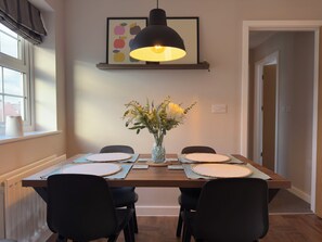 A dining area with a table set for four, a vase with flowers, and a pendant light. - Cosy coach house in Hereford (Hereford)