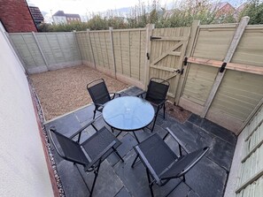 Eine Terrasse mit einem runden Tisch und vier Stühlen, umgeben von einem Holzzaun und einem Kiesbereich.