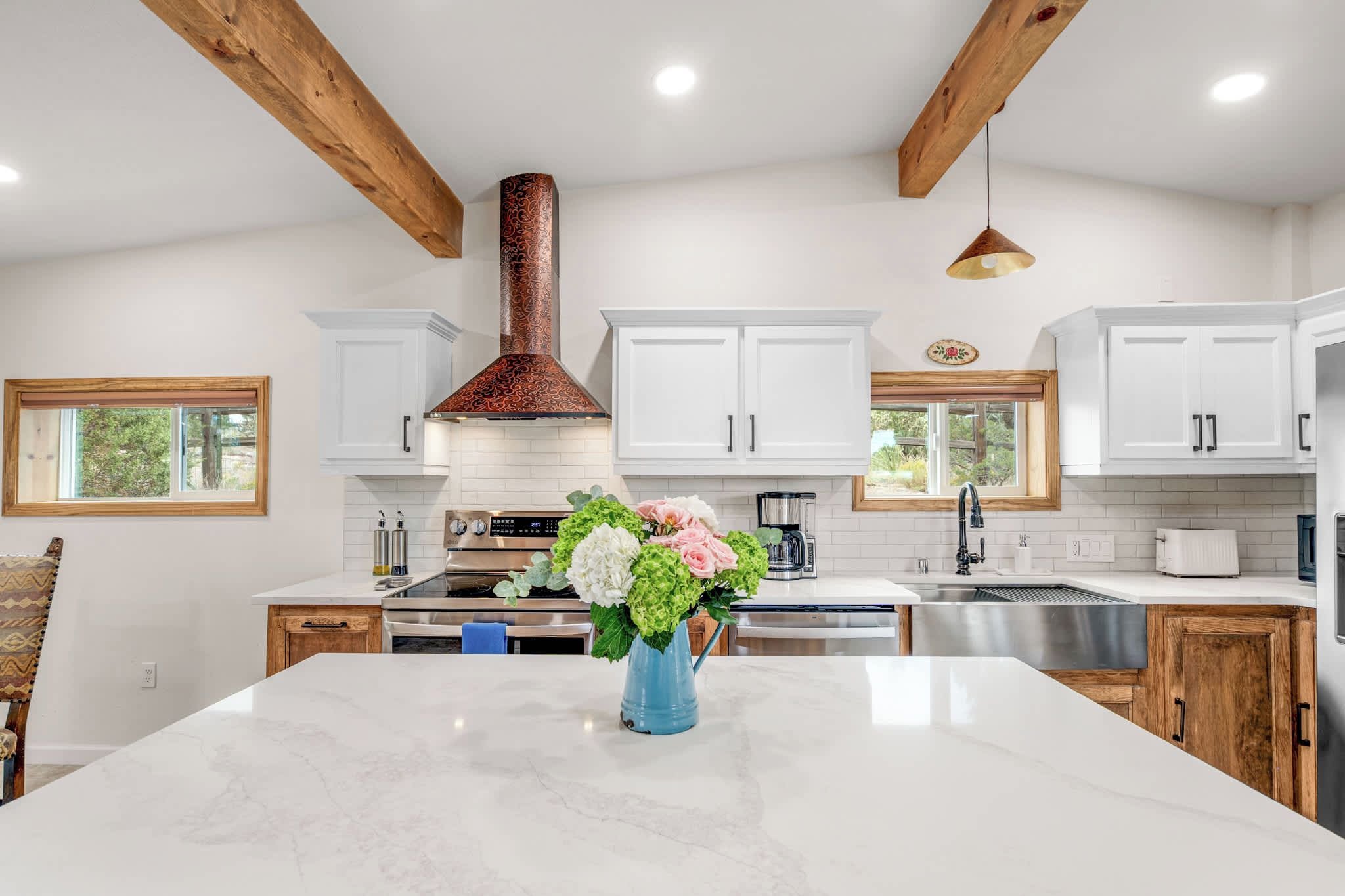 A modern kitchen with white cabinets, a marble island, and a copper range hood.