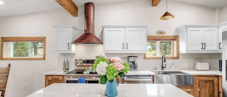 A modern kitchen with white cabinets, a marble island, and a copper range hood.