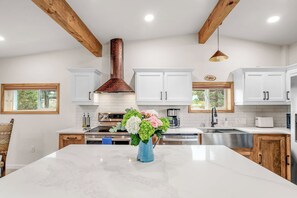 A modern kitchen with white cabinets, a marble island, and a copper range hood. - Renovated Horse Corral Hideaway (Santa Fe)