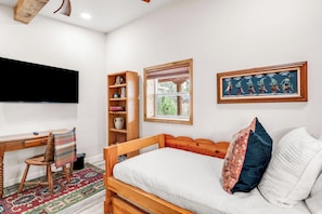 Ein Schlafzimmer mit einem Bett, einem Schreibtisch, einem Stuhl, einem Bücherregal, einem Fenster und einem an der Wand befestigten Fernseher.