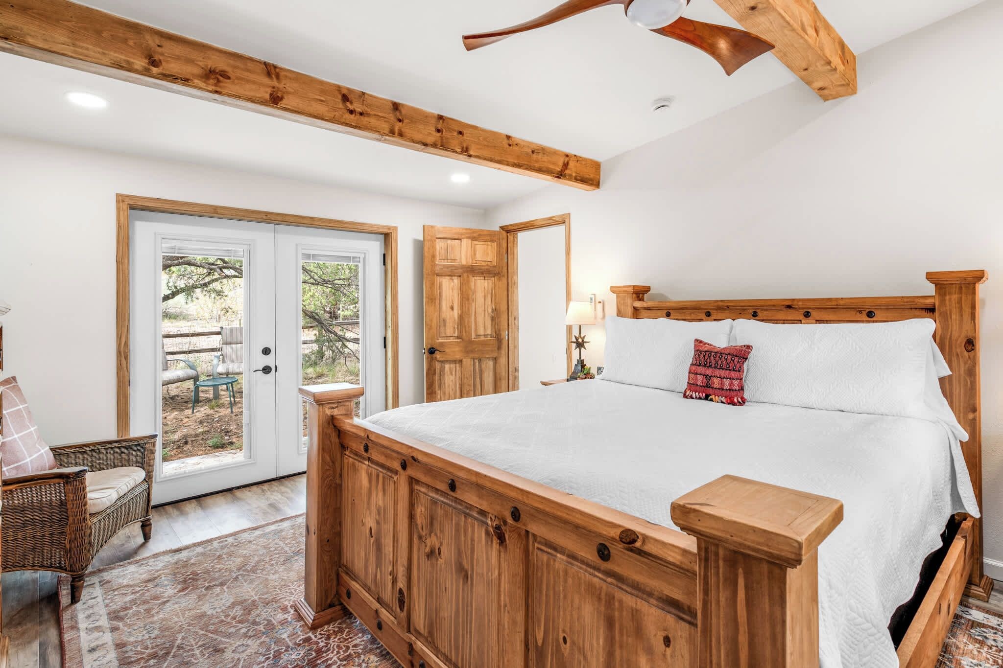 A bedroom with a wooden bed, a wicker chair, and a view through a glass door.