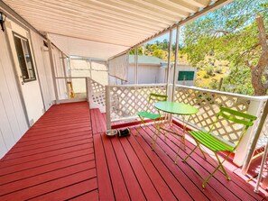A covered outdoor area with a red wooden floor, a green table, and a bench.