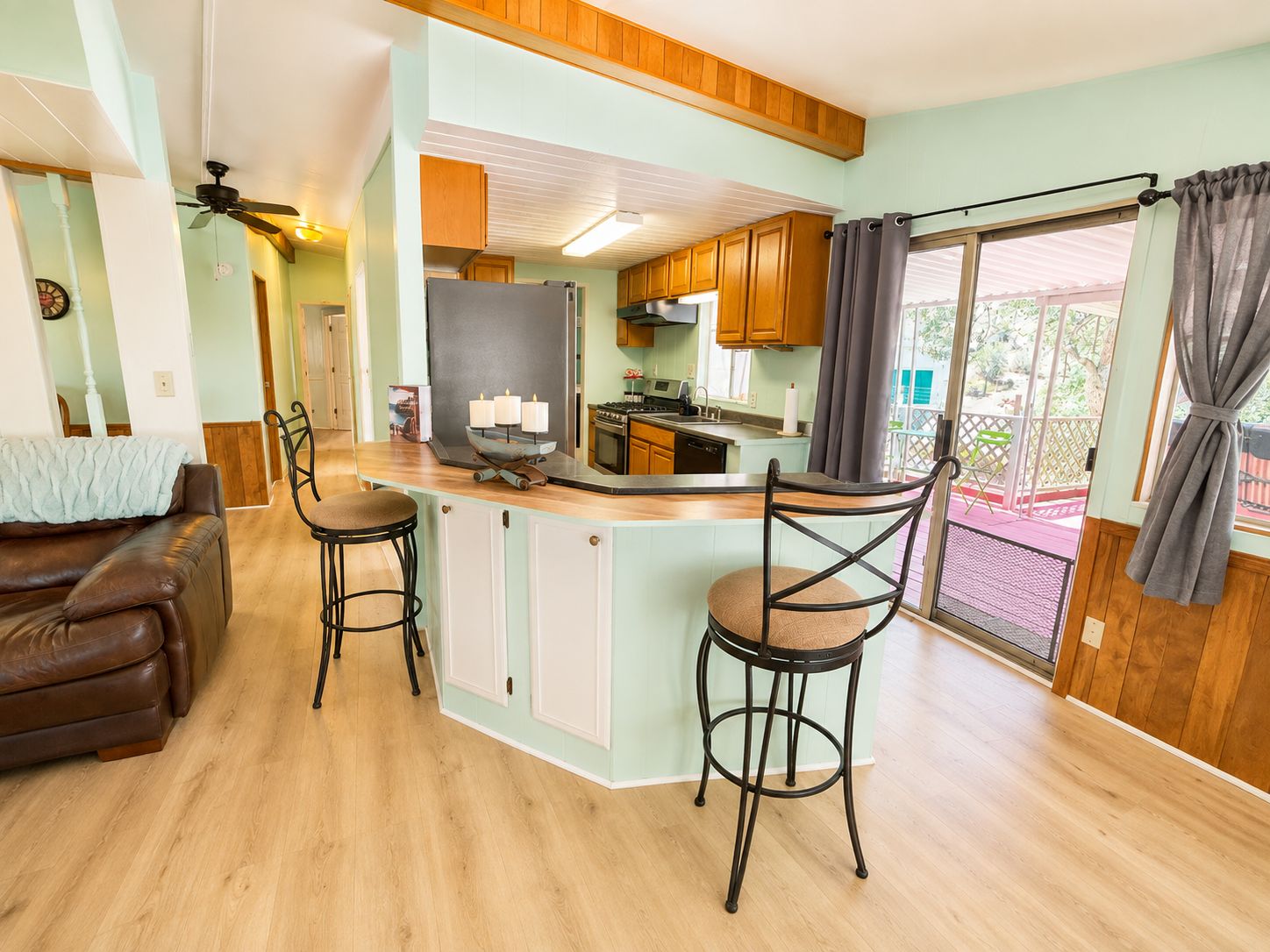 A kitchen with wooden cabinets, a bar area with stools, and a view of the outdoors.