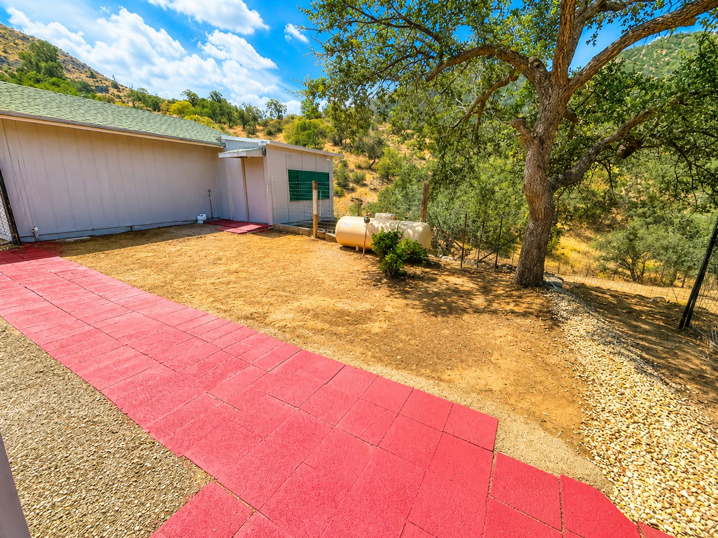 A building with a red paved area, a green door, and a tree in the background.