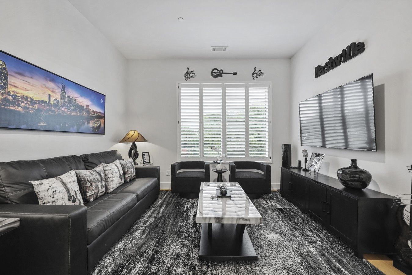A modern living room with a black leather sofa, a coffee table, and a cityscape painting.