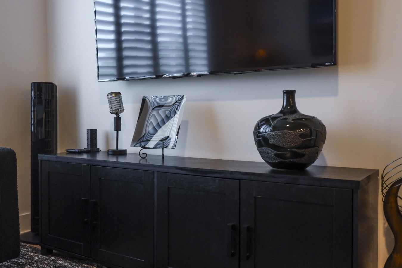 A black entertainment unit with a flat-screen TV mounted above it, a vintage microphone, and a decorative vase.