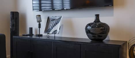 A black entertainment unit with a flat-screen TV mounted above it, a vintage microphone, and a decorative vase.