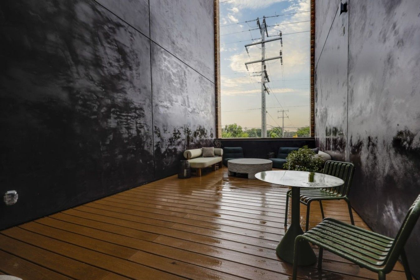A room with a wooden floor, a sofa, a round table, and a chair. There is a view of power lines and trees through the window.