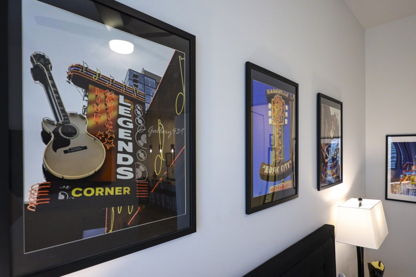 Obra enmarcada en una pared, que incluye una guitarra y un paisaje urbano.