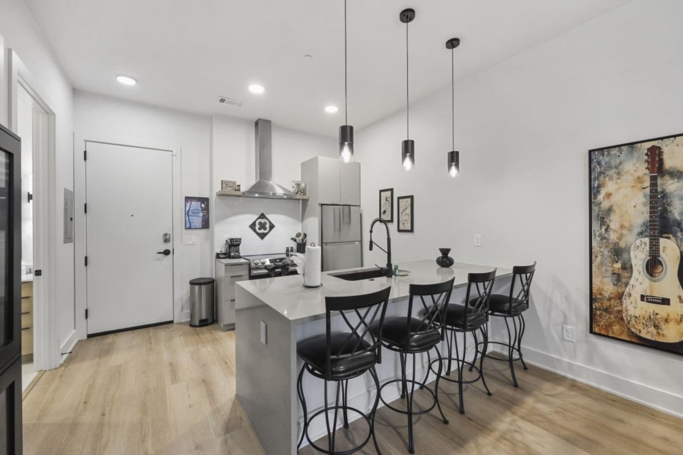 Une cuisine moderne dotée d’un îlot central, de luminaires suspendus et d’un coin repas avec des tabourets de bar.
