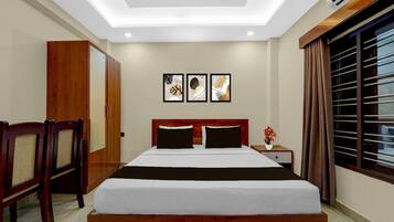 A hotel room with a bed, a wooden wardrobe, a nightstand with a vase, and a window with curtains.