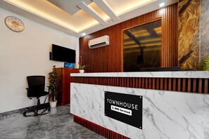 A reception desk with a marble top, a television mounted on the wall, and a sign indicating 'TOWNHOUSE OYO-Serviced'.
