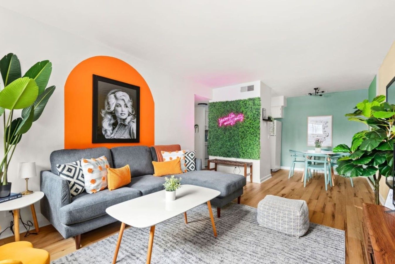 A modern living room with a grey sofa, a white coffee table, and a green wall with a neon sign.