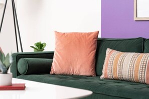 Ein grünes Sofa mit zwei Kissen, einer kleinen Topfpflanze und einem weißen Tisch mit einem roten Buch.