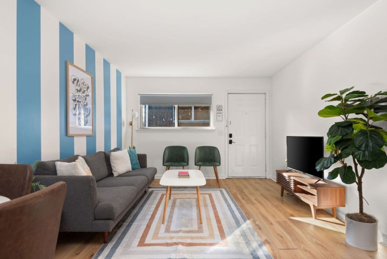 A living room with a sofa, two chairs, a coffee table, a TV, a plant, and a window with blinds.