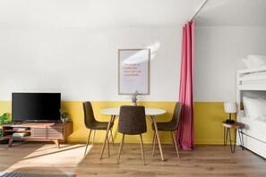 Ein Zimmer mit Fernseher, Tisch mit Stühlen, Etagenbett und einem gerahmten Zitat an der Wand.