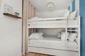 Una cama litera con ropa blanca, un estante con una planta y una lámpara fijada a la pared.