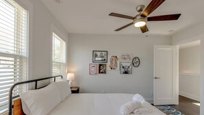 Une chambre à coucher comprenant un lit, un ventilateur de plafond, une table de chevet avec une lampe et des œuvres d’art murales.