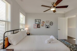 Un dormitorio con cama, ventilador de techo, mesita de noche con lámpara y decoración en la pared.