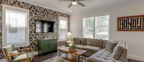 A living room with a sofa, a chair, a coffee table, a TV, and a ceiling fan.