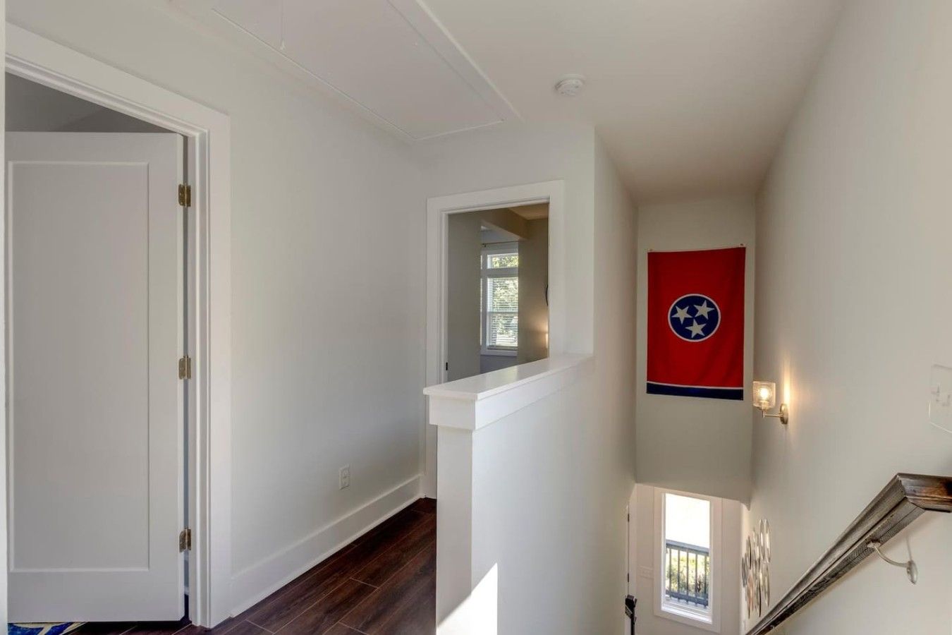 Un couloir aux murs blancs, avec un plancher en bois, une porte et un drapeau accroché au mur.