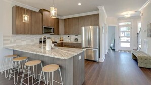 Une cuisine moderne dotée d’un îlot central, de tabourets de bar, d’appareils électroménagers en acier inoxydable et de meubles de rangement en bois.