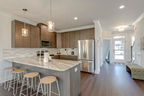 Una cocina moderna con una isla central, taburetes de bar, electrodomésticos de acero inoxidable y armarios de madera.
