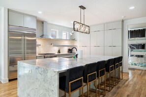 Een moderne keuken met een marmeren eiland, roestvrijstalen apparatuur en een hangende lamp.