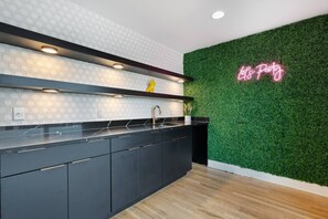 A modern kitchen with a black countertop, a stainless steel sink, and a neon sign on the wall. - Last Call Lounge | Rooftop Skyline + Game Room (Nashville)