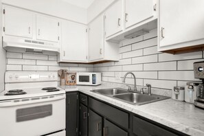 A kitchen with white cabinets, a stove, a microwave, and a sink. - The Lyric - #103 & #104 | Two Suites on Music Row (Nashville)