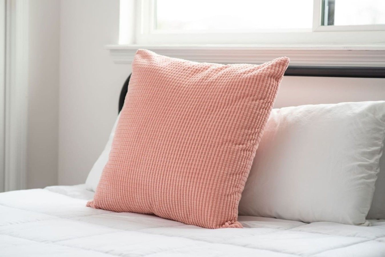 A bed with a white mattress and a single pink pillow.