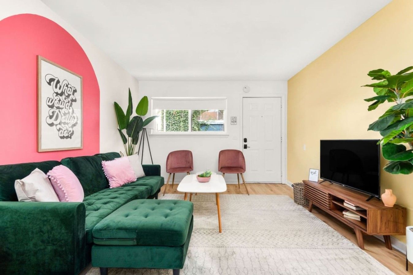 Una sala de estar con un sofá verde, una mesa de centro blanca y un mueble para televisión.