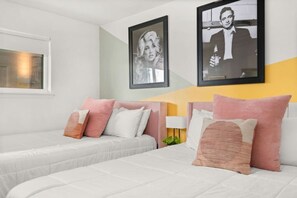 A hotel room with two beds, each with pink and white bedding, a bedside table with a lamp, and two framed pictures on the wall. - The Lyric - #201 & #202 | Two Suites on Music Row (Nashville)