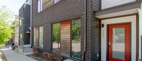 A modern two-story apartment building with a brick facade, large windows, and a red door.